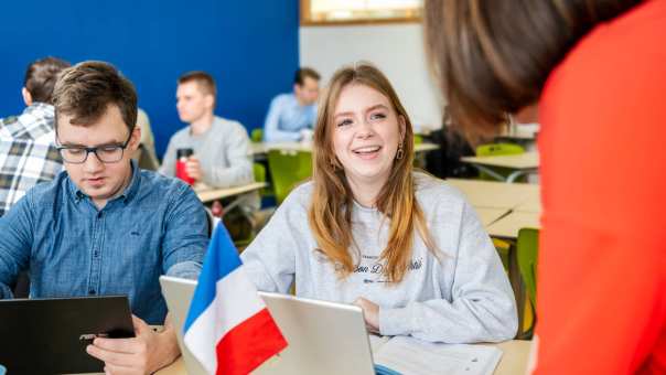Studente Leraar Frans met een grijze trui lacht met haar mond open naar haar docent.