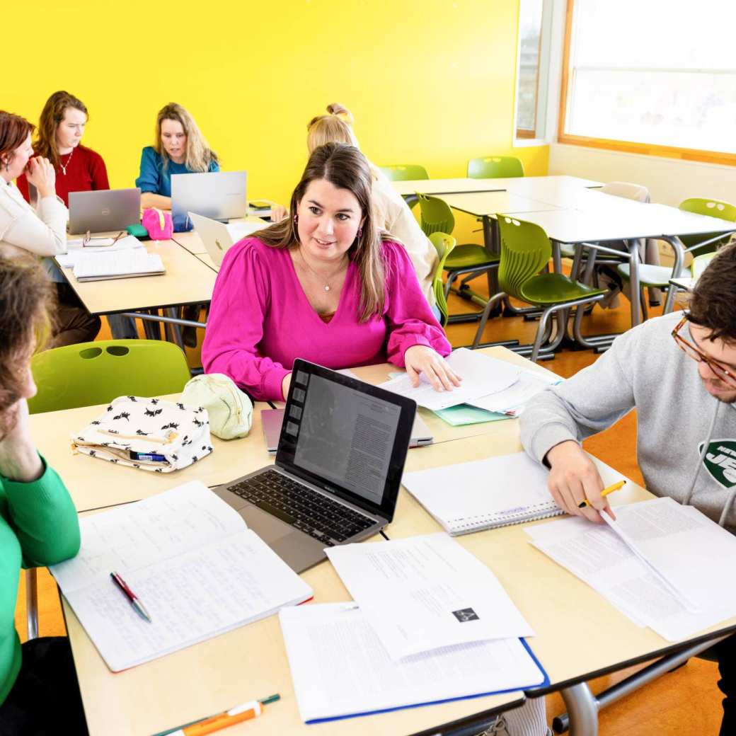 Studenten werken aan tafels waar boeken en laptops op liggen