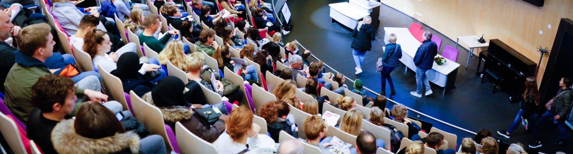 Beeld van bovenaf in auditorium met volle zaal voor presentatie