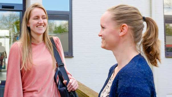 drie vrouwen staan samen buiten, in gesprek. Roze trui is aan het lachen.