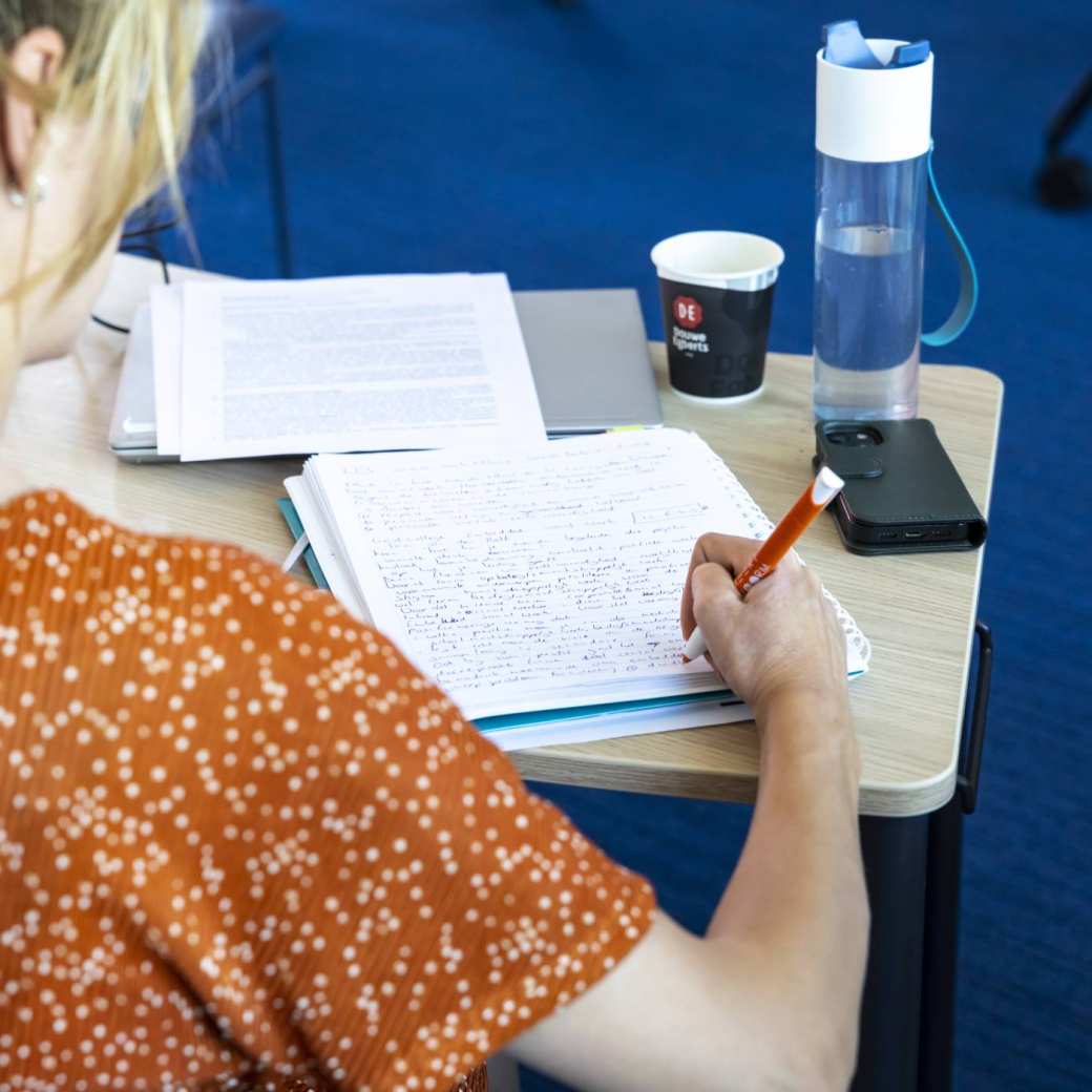 Student van de Master Social Work maakt aantekening met pen en papier.