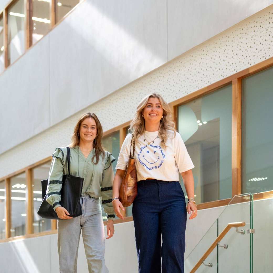 Twee studenten lopen door de gang van K35 en komen via de trap. 