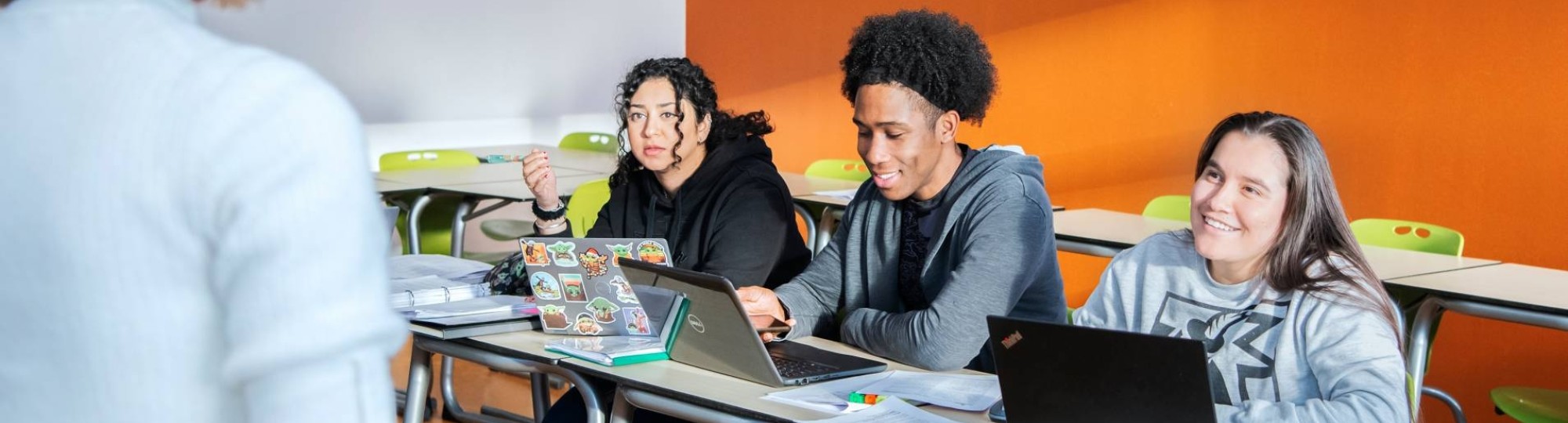 Docent zit op een tafel en geeft uitleg aan 3 masterstudenten die lachen