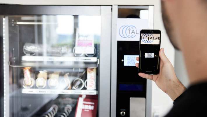 Man betaalt bij de snackautomaat met de GNU-taler app op zijn telefoon