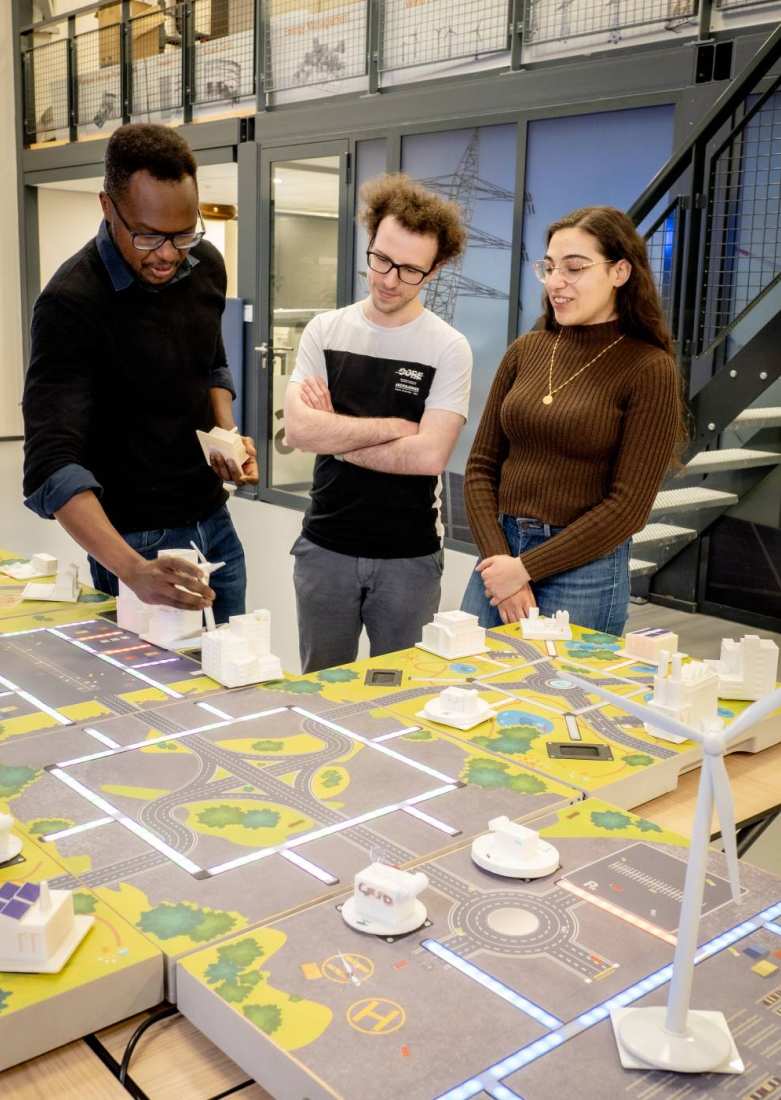 Twee studenten van de Master Engineering Systems Sustainable Energy en een docent bij de Smart Grid-demotafel.