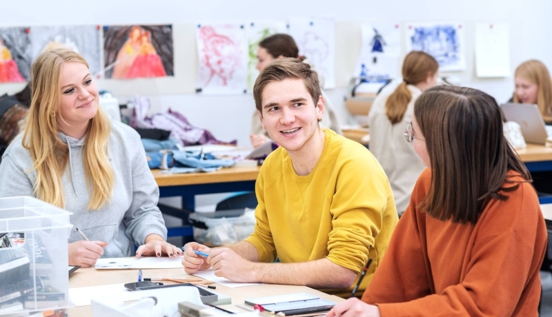 Fotoshoot maakdagen beeldende vorming 2022.Drie studenten met elkaar in overkeg tijdens de les beeldende vorming. De jongen in het midden lacht