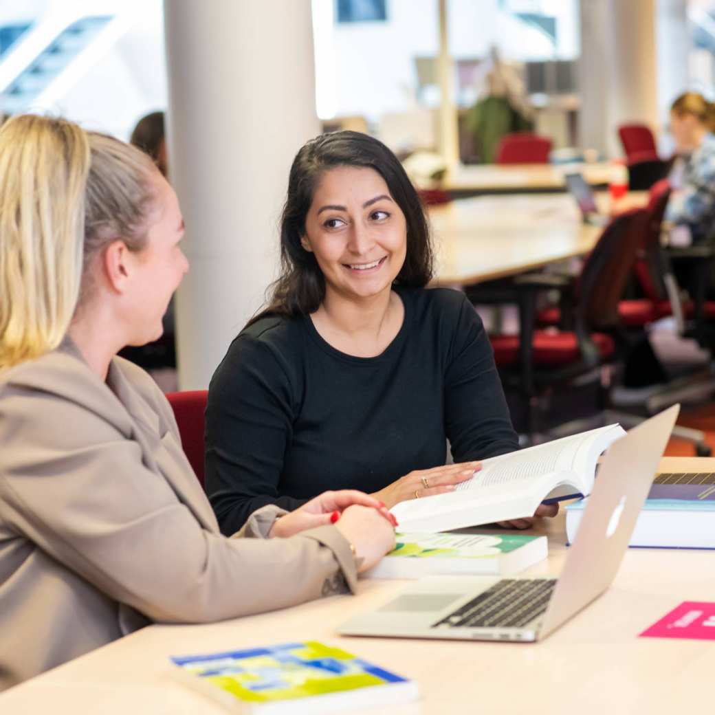 Twee studenten in de bibliotheek aan het overleggen voor de studie PMT deeltijd