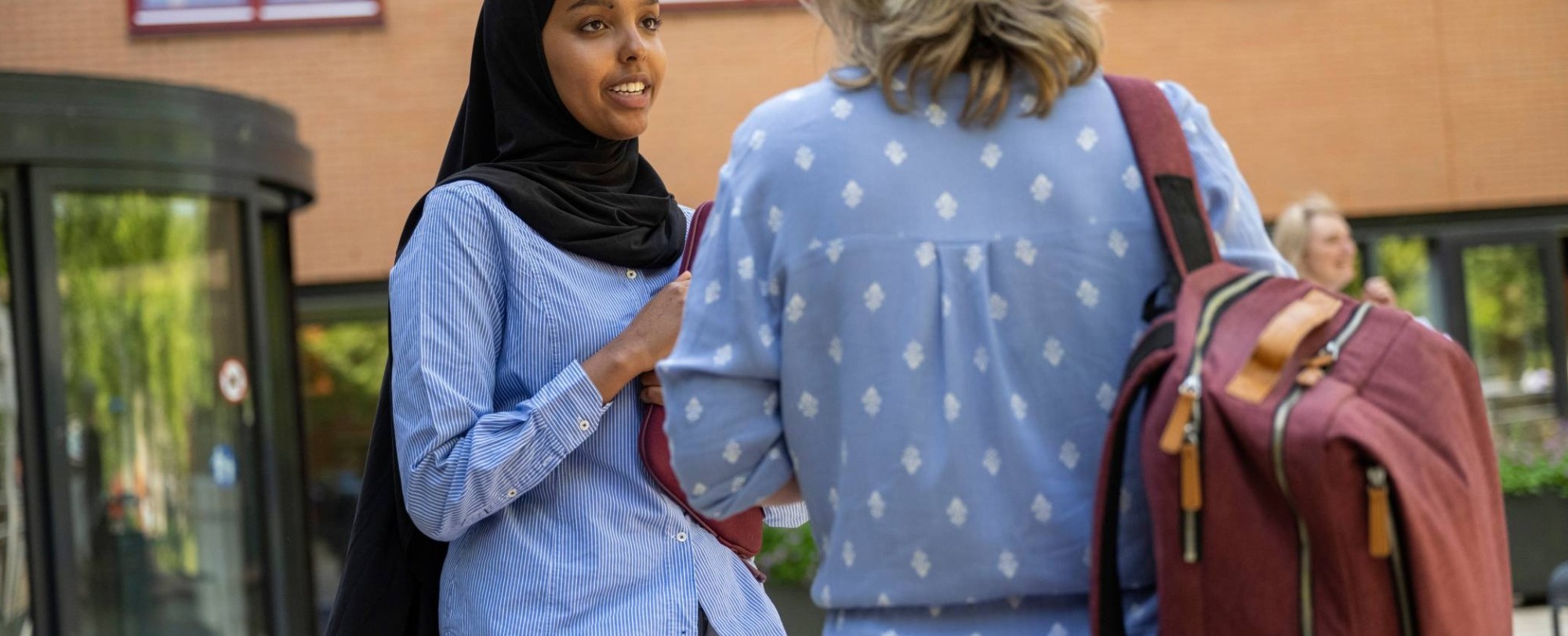 Student met hoofddoek praat buiten met docent, studentbegeleiding, bij K33.