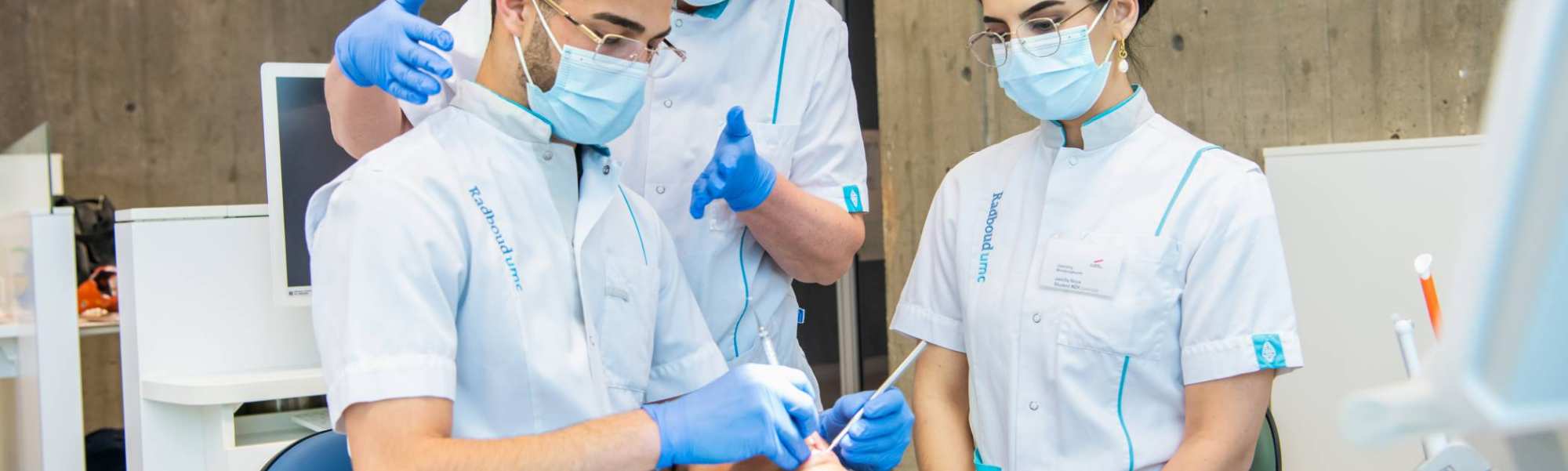 Docent helpt een student tijdens een behandeling, een andere student kijkt toe.