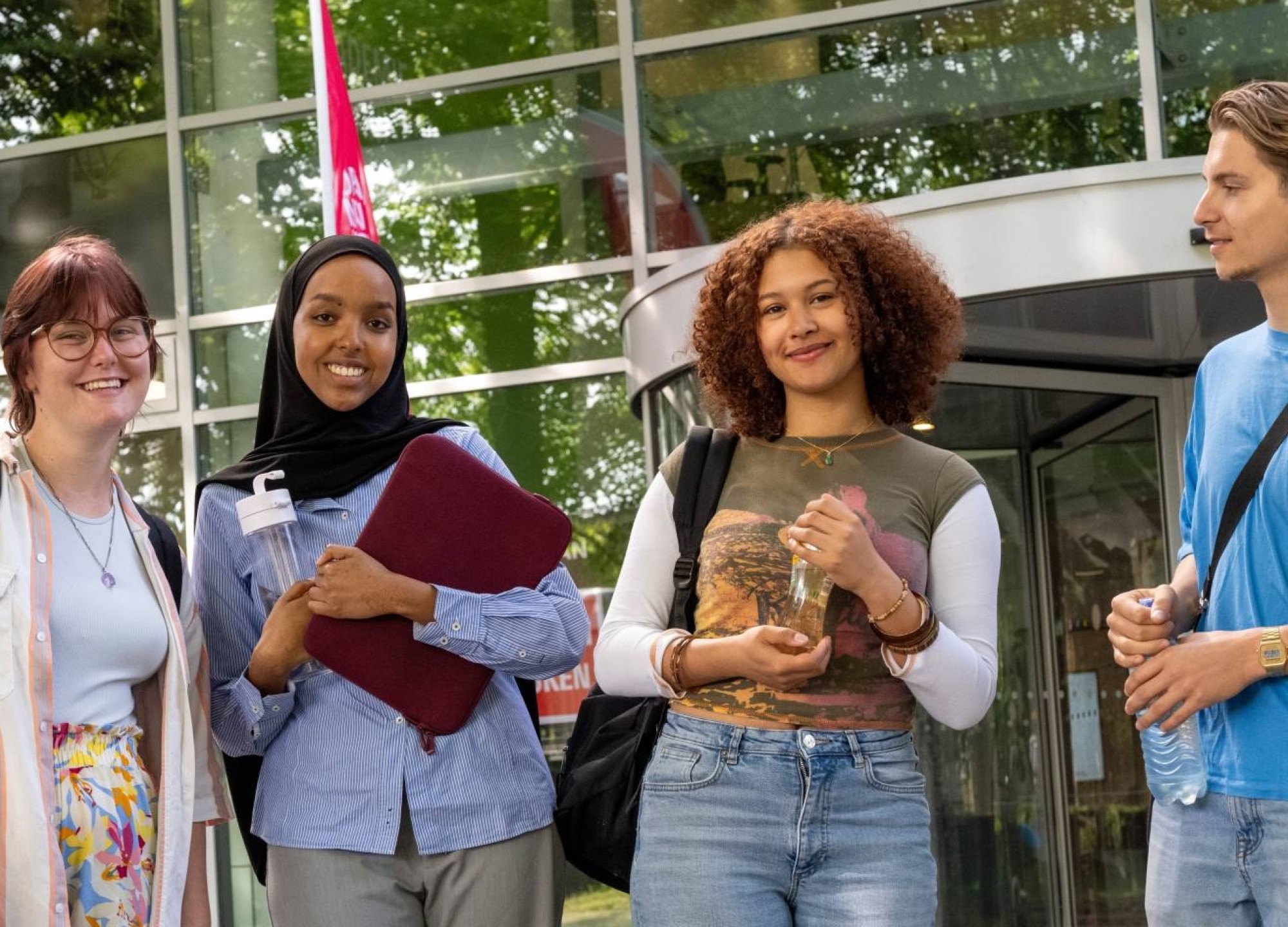 Vier studenten staan bij gebouw LvS10 bij draaideur, buiten. Op een rijtje. 