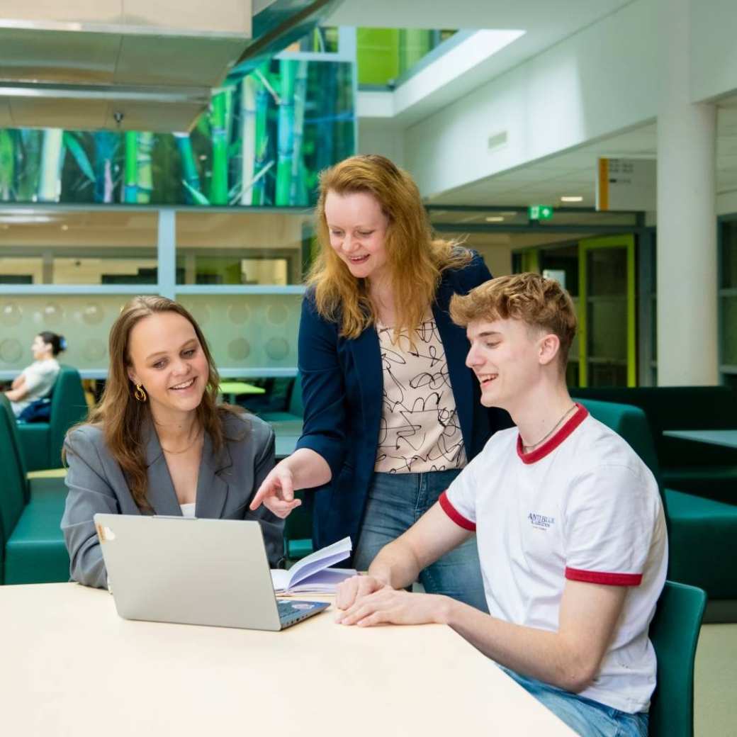 Studenten hbo Bedrijfskunde werken aan een praktijkopdracht en krijgen uitleg van een docent