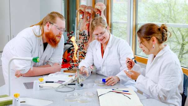 Docent en twee studenten doen een proefje met petrischaaltjes in het lab.