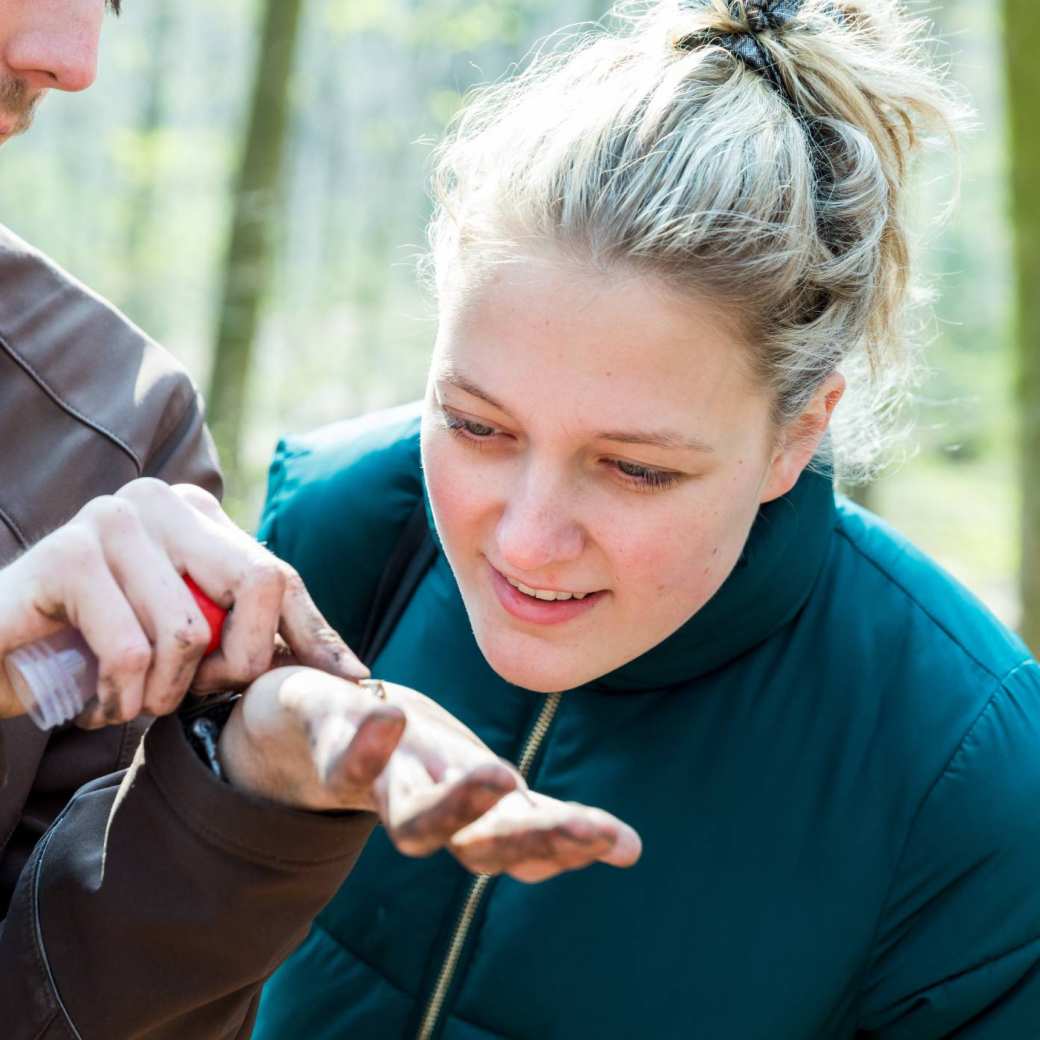 Biologie student met petrol jas kijkt enthousiast naar kleine voorwerp