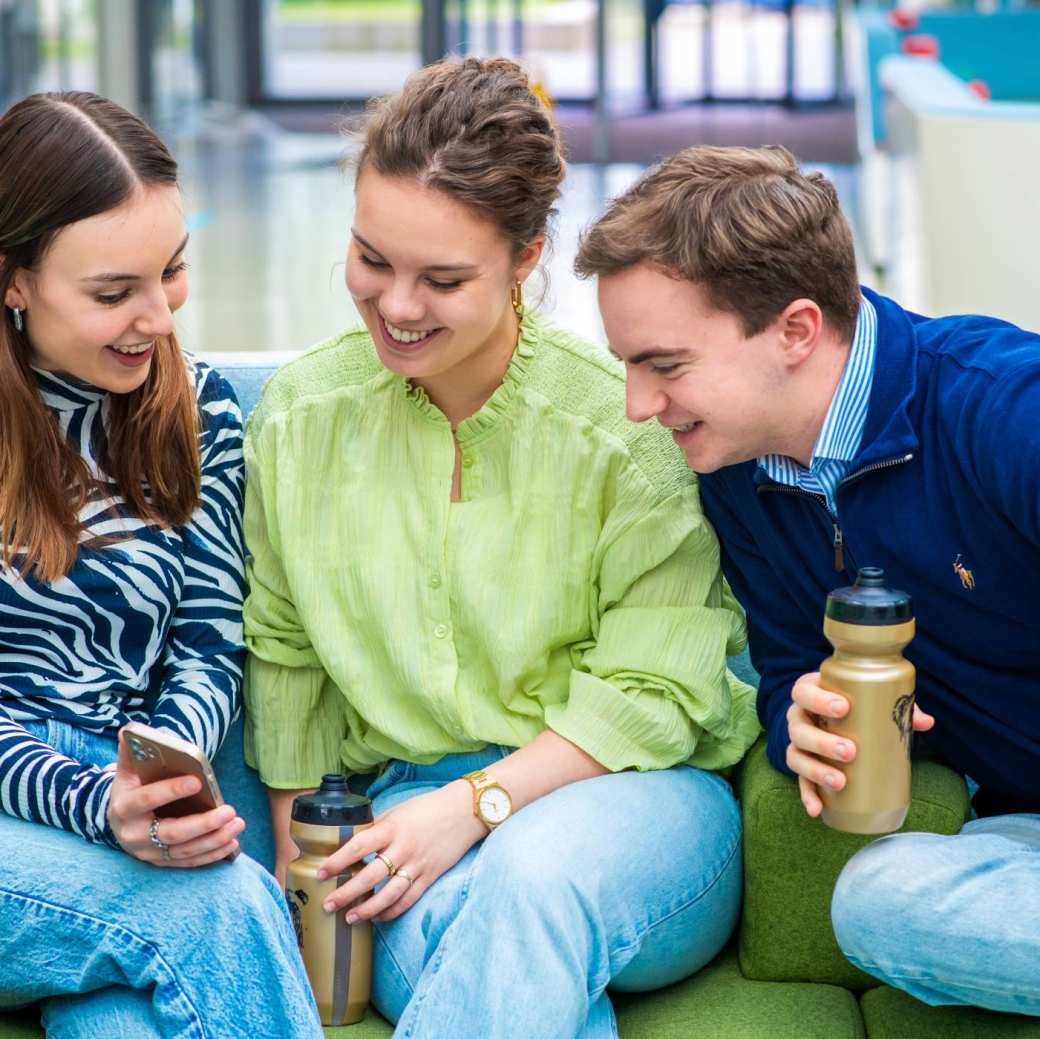 drie studenten kijken samen op één mobiel