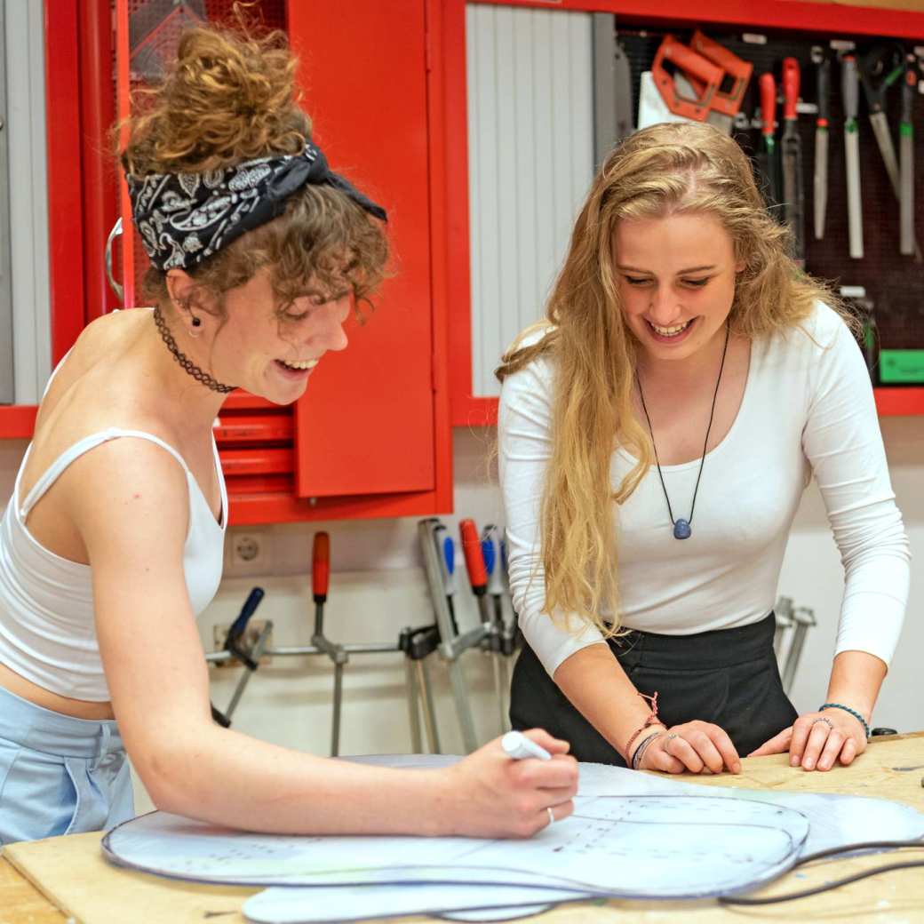 Twee beeldende therapie studenten werken samen aan een project in houtlokaal tijdens een praktijkles