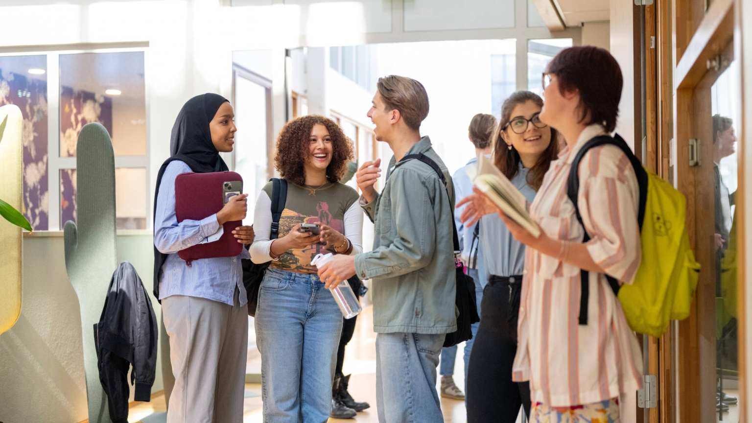 Een groepje studenten staan te wachten voor de klas en hebben plezier. 