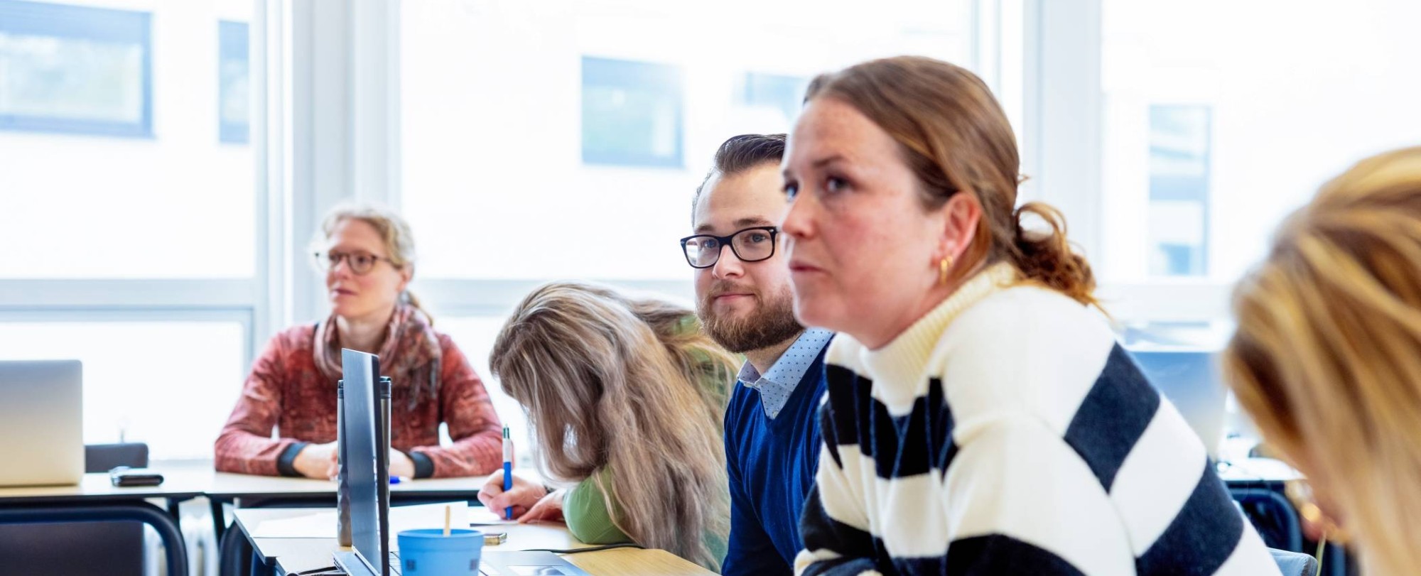 Drie mensen met elkaar pratend aan een tafel. De vrouw in de gele trui lacht tijdens het gesprek