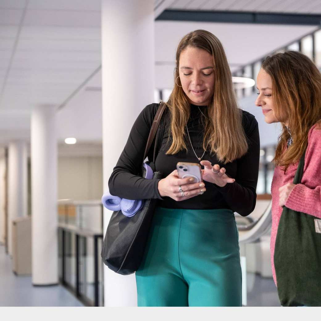 2 studenten met tas kijken op mobiel in de gang.