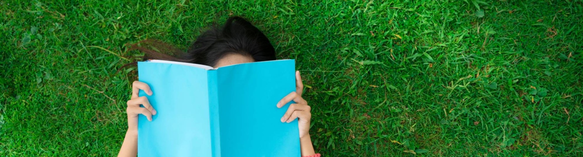 Jongere leest een boek in het gras