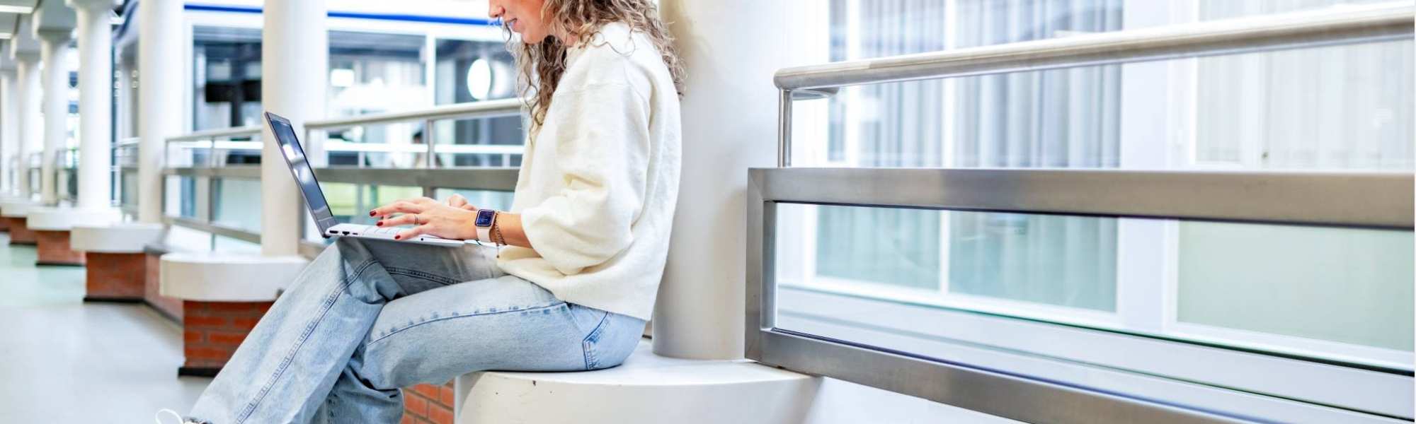 Student van de bachelor Commerciële Economie deeltijd, duaal in gang met laptop. 