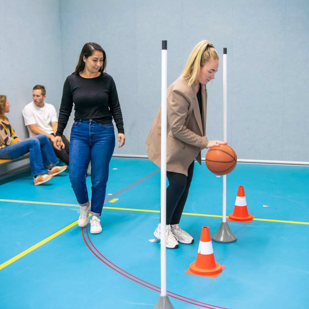 Twee studenten waarbij één student met een bal aan het slalommen is