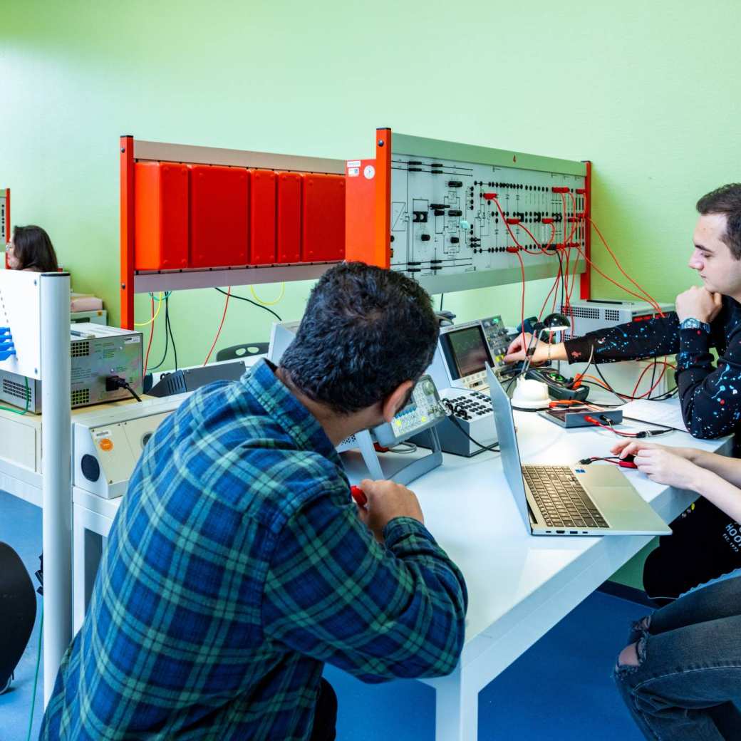 Een elektrotechniekdocent kijkt mee met studenten tijdens practicum.