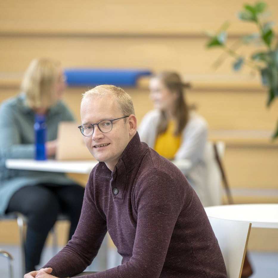 Mannelijke student zit op stoel en kijkt lachend in de camera