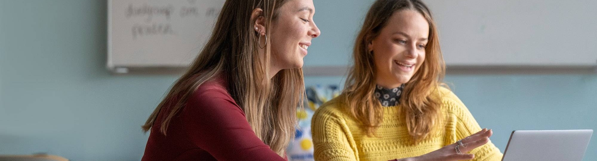 Twee deeltijdstudenten overleggen lachend met elkaar in de klas.