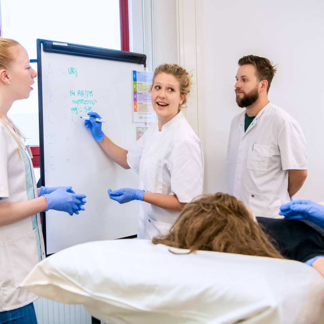 3 studenten en instructeur overleggen met elkaar bij bord