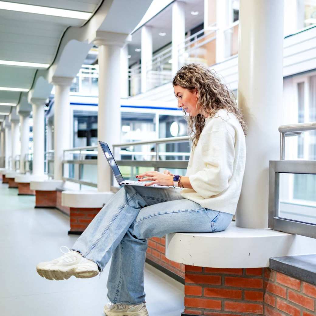 Student van de bachelor Commerciële Economie deeltijd, duaal in gang met laptop. 