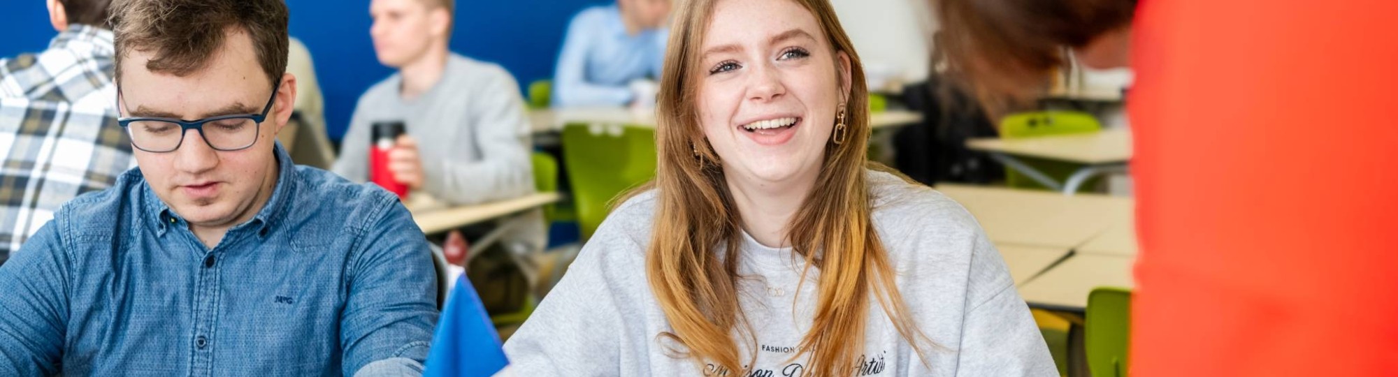 Twee studenten zitten in de mediatheek en kijken lachend naar de laptop die voor hun staat.