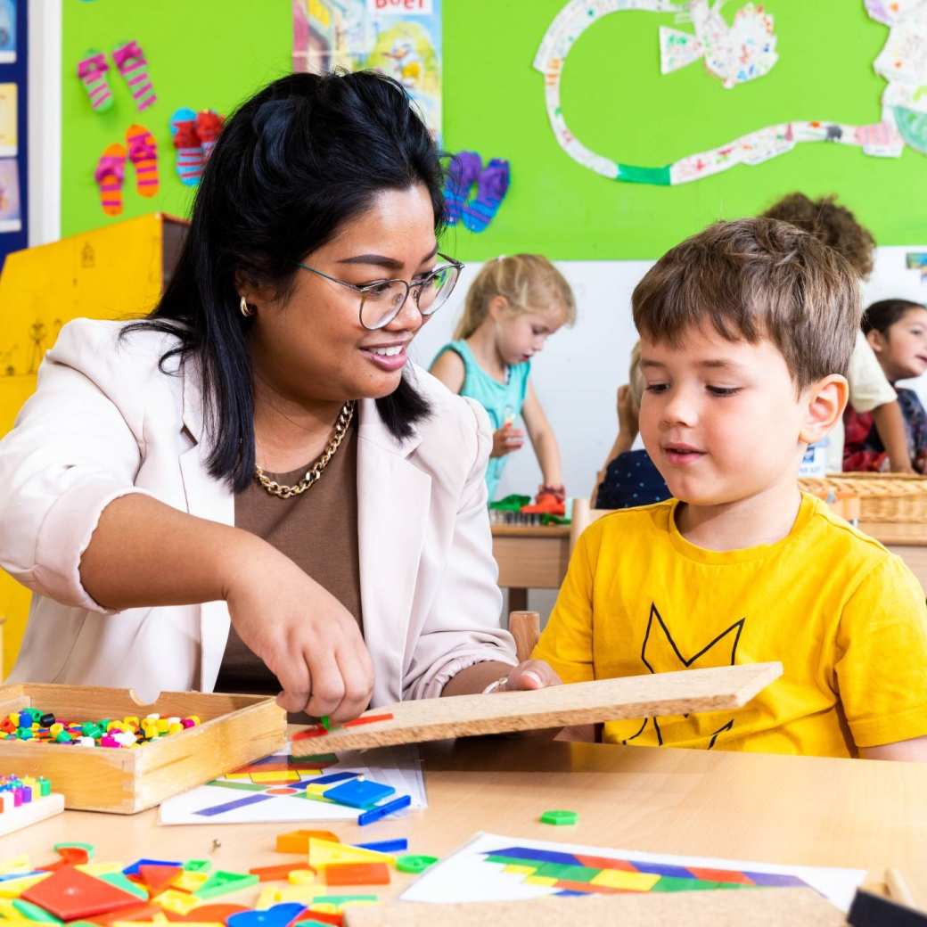 De juffrouw helpt een leerling met het leggen van een puzzel