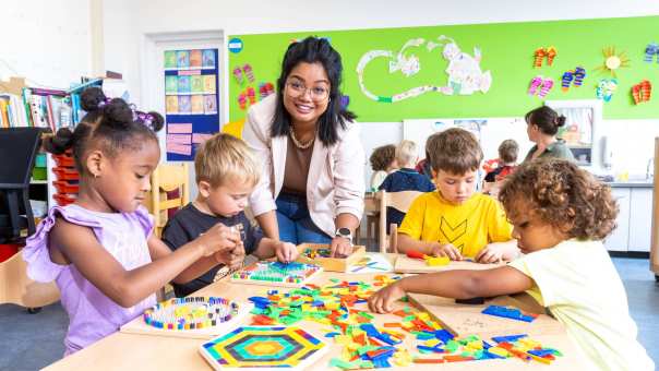 De kinderen in de klas leggen een puzzel en de lerares van de opleiding leraar basisonderwijs helpt hen hierbij.