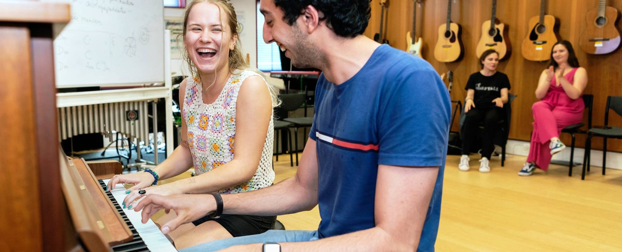 Twee studenten muziektherapie spelen samen op de piano tijdens een praktijkles