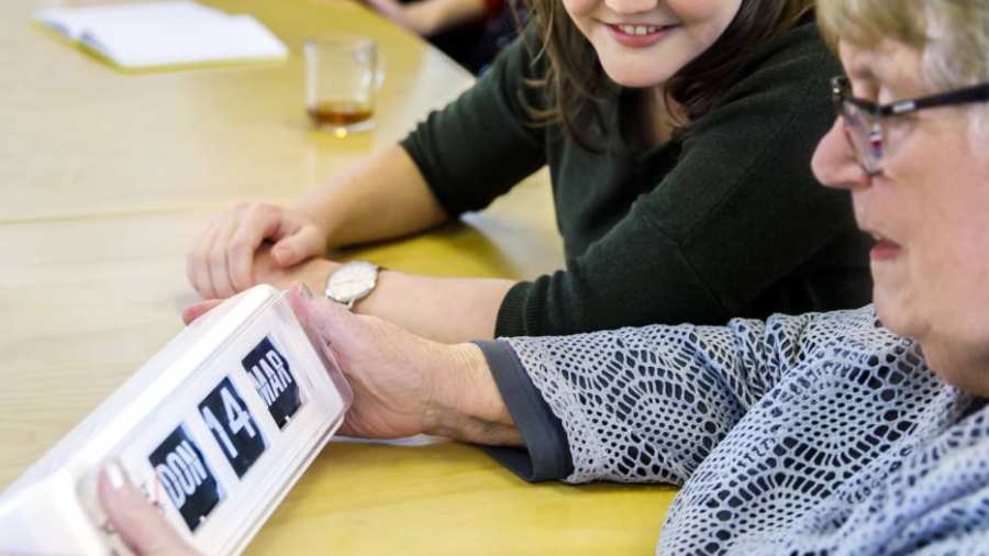 bijeenkomst wijkatelier lindenholt- aan tafel studente met oudere vrouw en kalanderklok