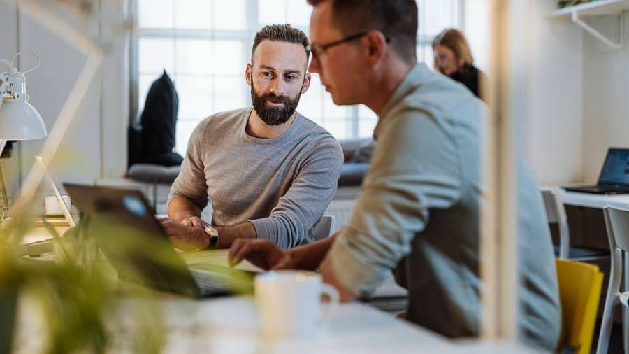 Twee mannen zitten aan een bureau en zijn in overleg in een kantoorruimte.