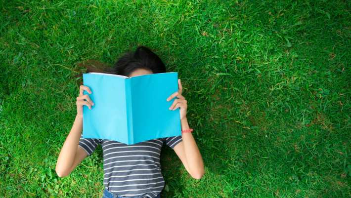 Jongere ligt in het gras en leest boek