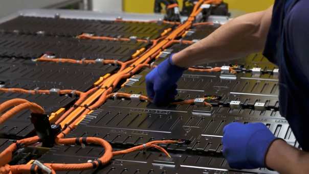 Monteur met grijze handschoenen aan de slag met een batterij met oranje draden. Seece - SEE- elektrotechniek, werktuigbouwkunde