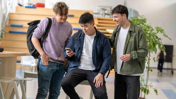 Drie jongens staan in de hal en kijken samen op een telefoon. 