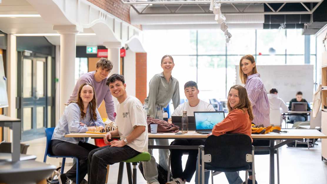 Groep studenten aan het werk aan een project, kijken in de camera en hebben plezier. 