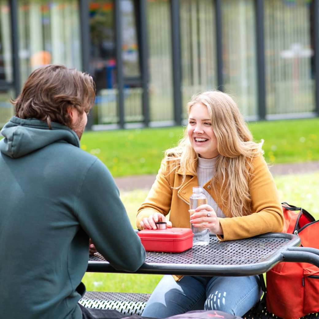 twee studenten buiten lachend aan picknicktafel