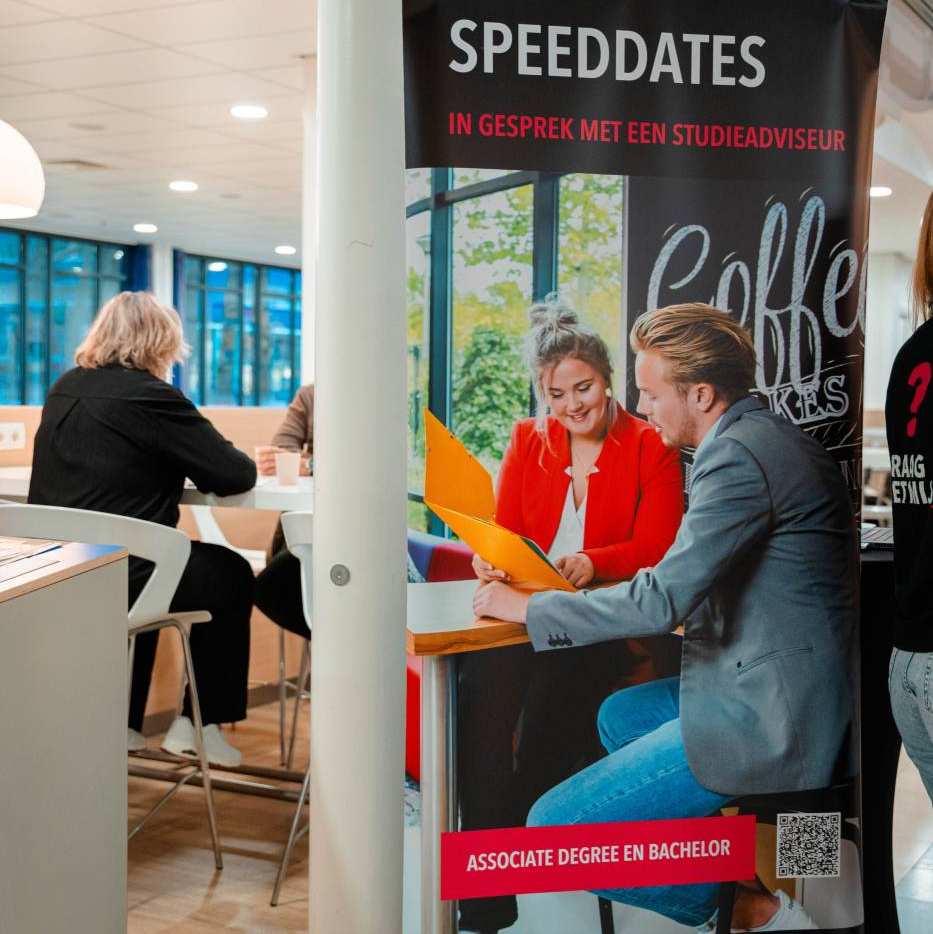 Adviseur achter een tafel op de open avond van de associate degree Bedrijfskunde deeltijd