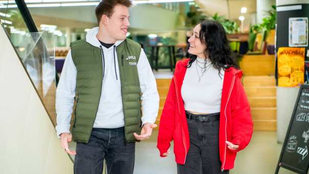 Twee studenten lachen naar elkaar tijdens het wandelen door de school.
