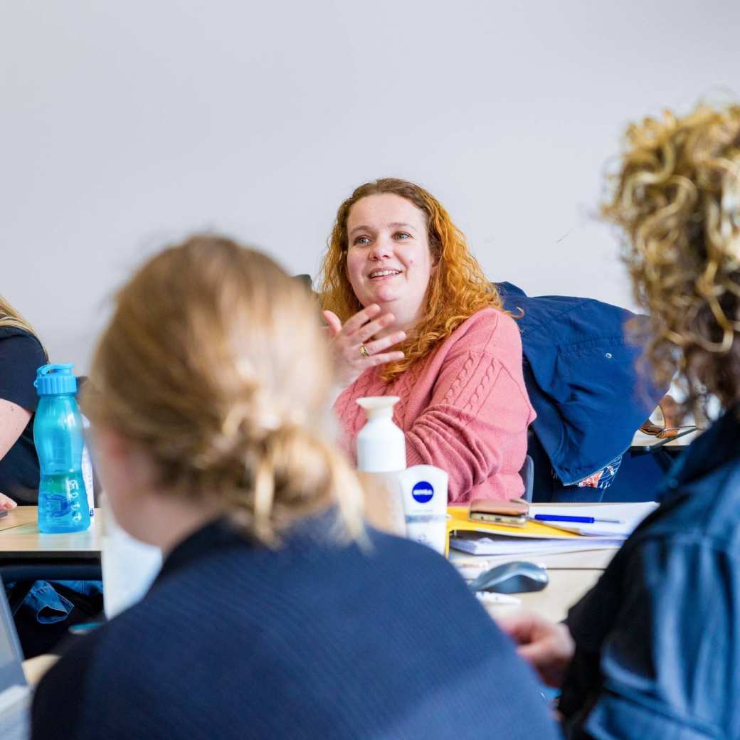 Vrouw in roze trui is in gesprek met docent tijdens de cursus acute pijn service.