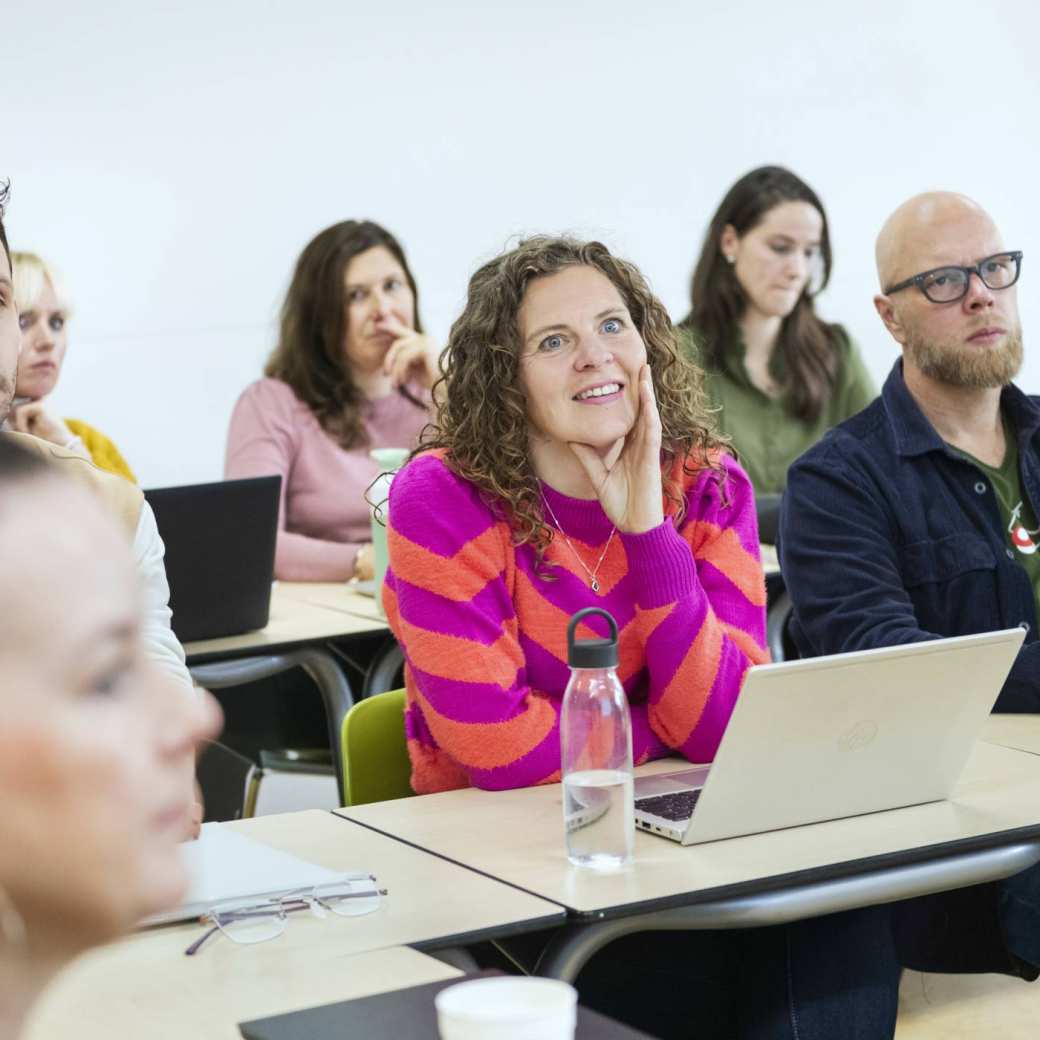 Klaslokaal gevuld met studenten die op een rijtje zitten en luisteren/kijken richting de docent.