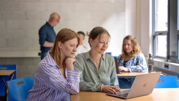 Twee studenten zijn samen aan het werk op de laptop, in de klas. 