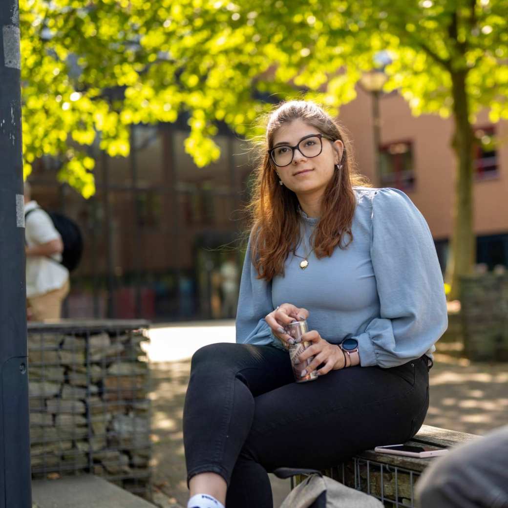 Portretfoto van studente buiten zittend op een bankje bij K33, in de pauze. 