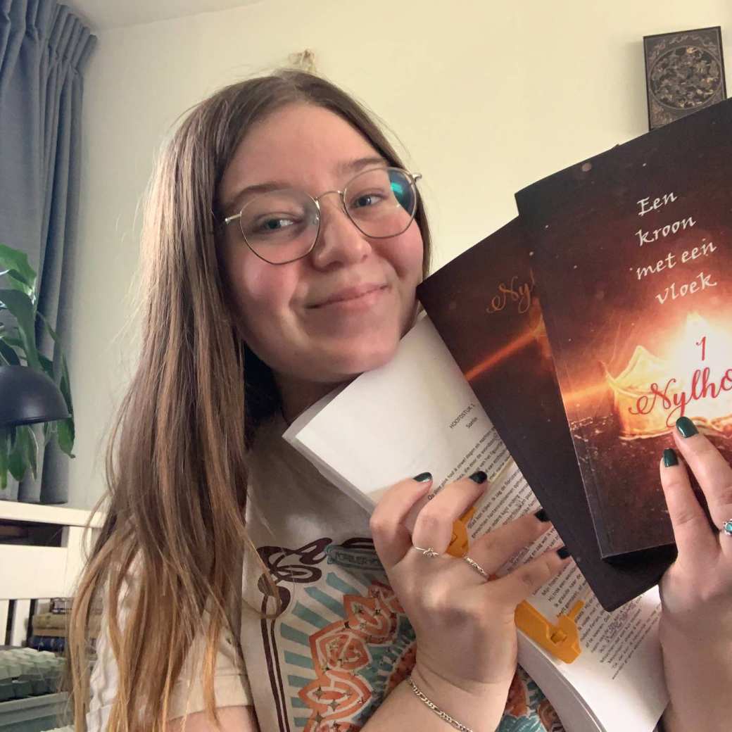 CMD-student Jade Vermeulen heeft haar eigen geschreven boeken in haar handen en glimlacht