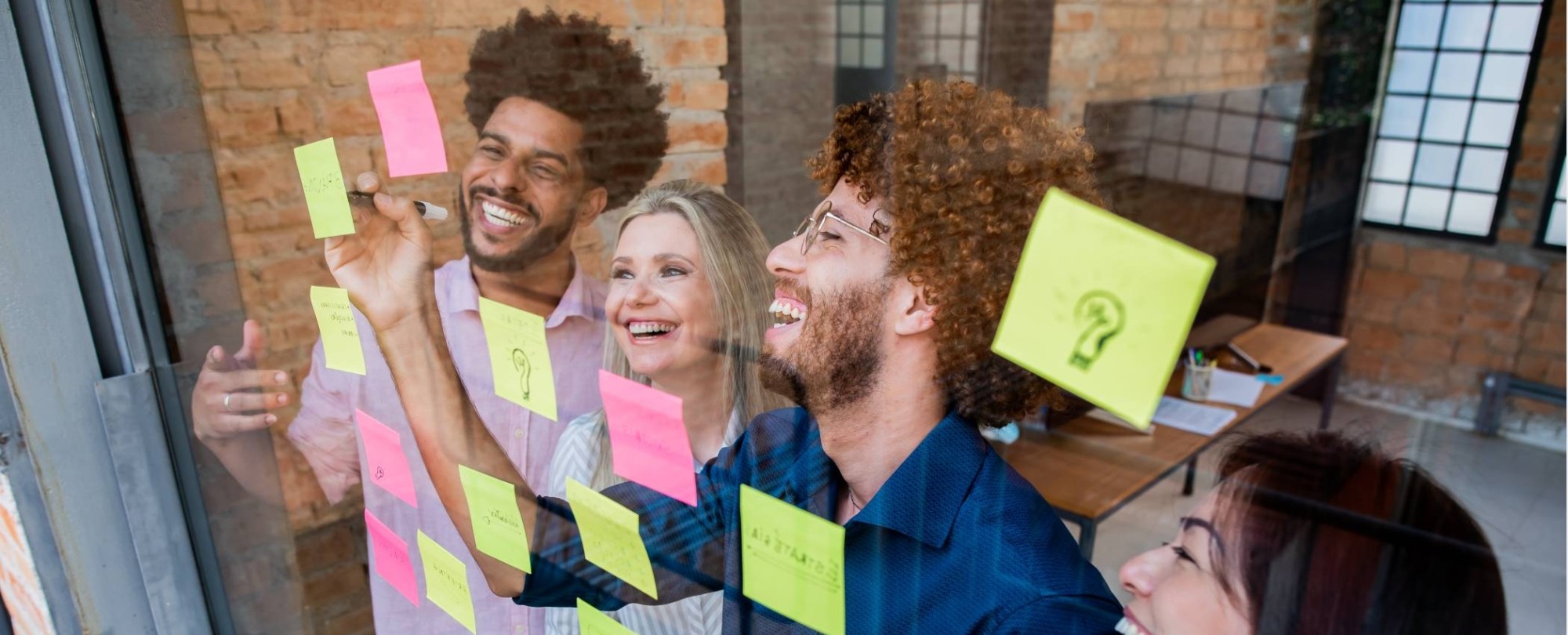 Groep jonge mensen plakken post-its op een glazen wand in een kantoor
