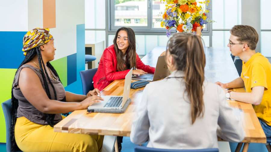 Groep van 4 studenten in overleg aan tafel in algemene ruimte HAN. 